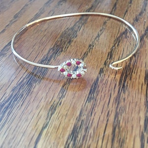 May include: A gold bangle bracelet with a red and white jeweled design. The design is a circle with red stones and white pearls.