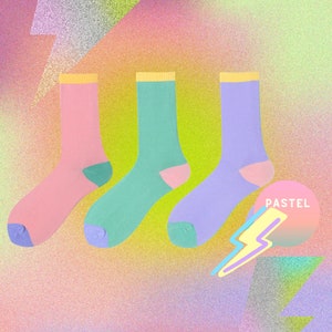 Könnte beinhalten: Drei Paar pastellfarbene Socken. Die Socken sind rosa, hellblau und hellgrün. Die Socken sind in einer Reihe auf einem glitzernden Hintergrund angeordnet.