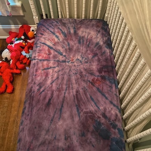May include: A purple and blue tie-dye fitted crib sheet with a swirling pattern.