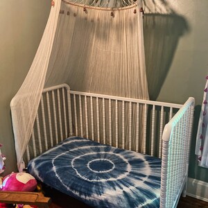 May include: White wooden crib with a white canopy and a blue tie-dye fitted sheet.