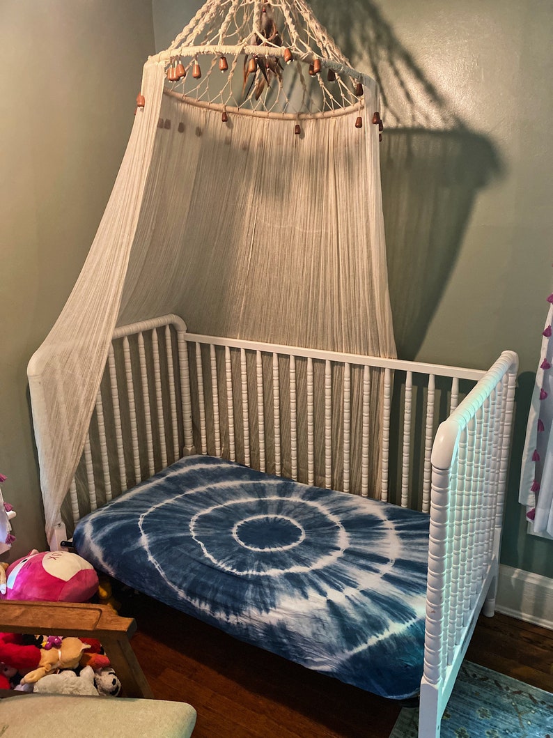 May include: White wooden crib with a white canopy and a blue tie-dye fitted sheet.