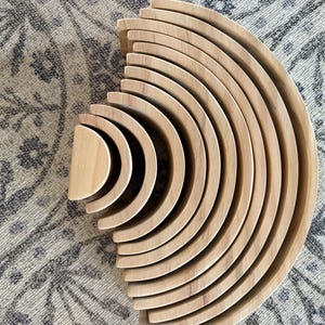 Puede incluir: Juguete apilable de arcoíris de madera con múltiples piezas curvas de varios tamaños. El juguete de madera natural está dispuesto en semicírculo, mostrando las diferentes capas. Diseñado para el juego y la educación de los niños.