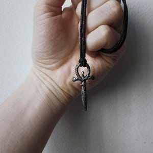 May include: A silver pendant necklace with a dagger-shaped ankh symbol on a black cord.