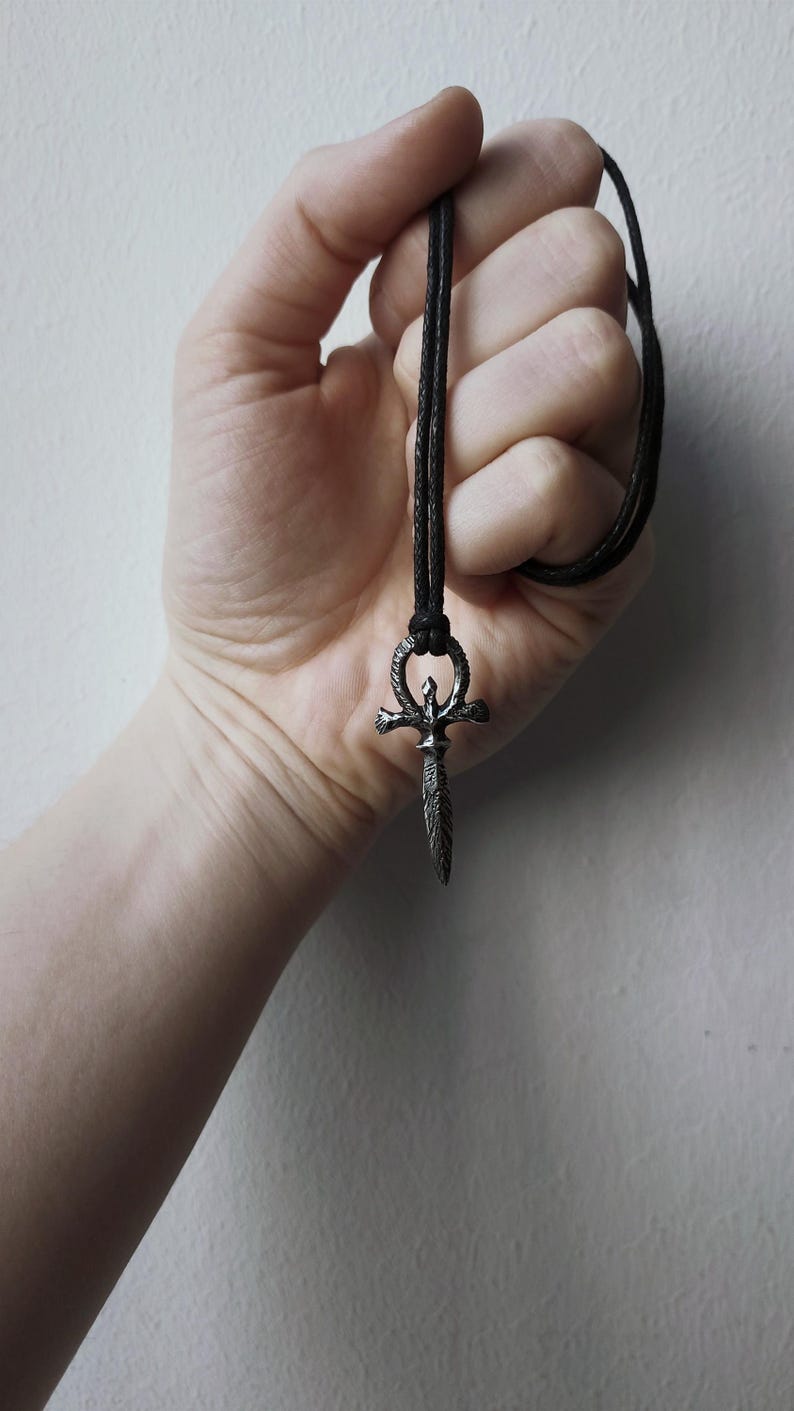 May include: A silver pendant necklace with a dagger-shaped ankh symbol on a black cord.