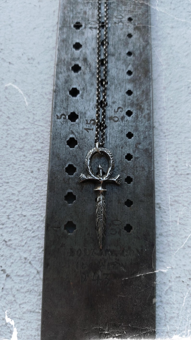 May include: A silver chain necklace with a silver ankh pendant. The ankh is a symbol of life and immortality in ancient Egyptian religion.