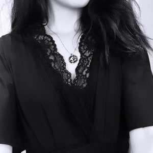May include: A black dress with a lace neckline and a silver chain necklace with a round pendant.