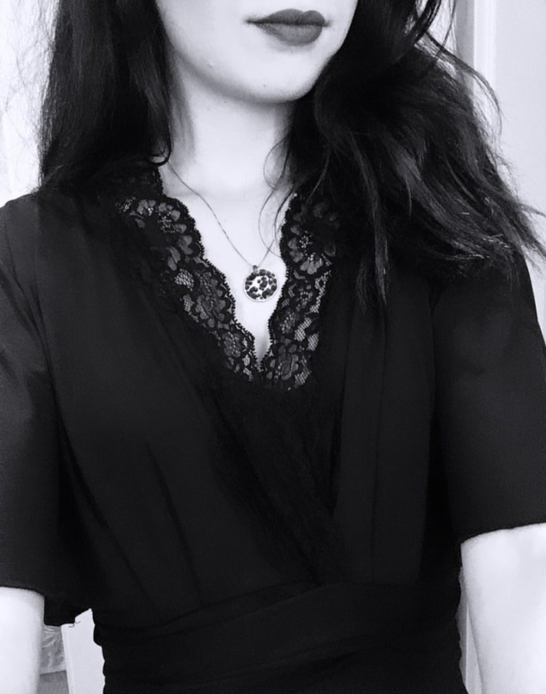 May include: A black dress with a lace neckline and a silver chain necklace with a round pendant.