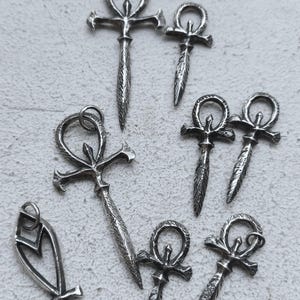May include: A collection of silver Ankh pendants, some with a cross design, on a white background.