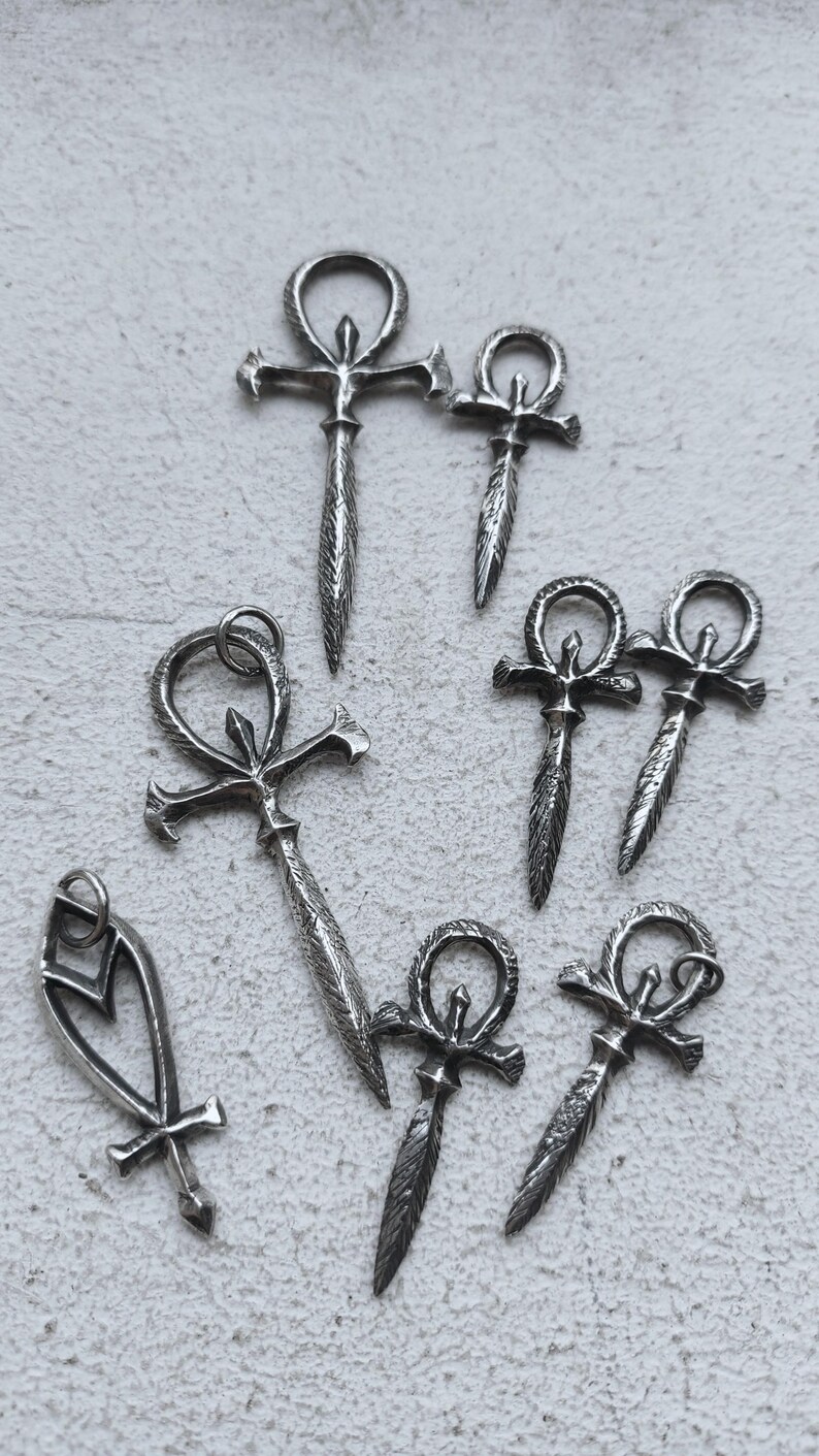 May include: A collection of silver Ankh pendants, some with a cross design, on a white background.