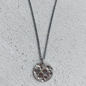 May include: A silver necklace with a round pendant featuring a textured surface with raised circles.