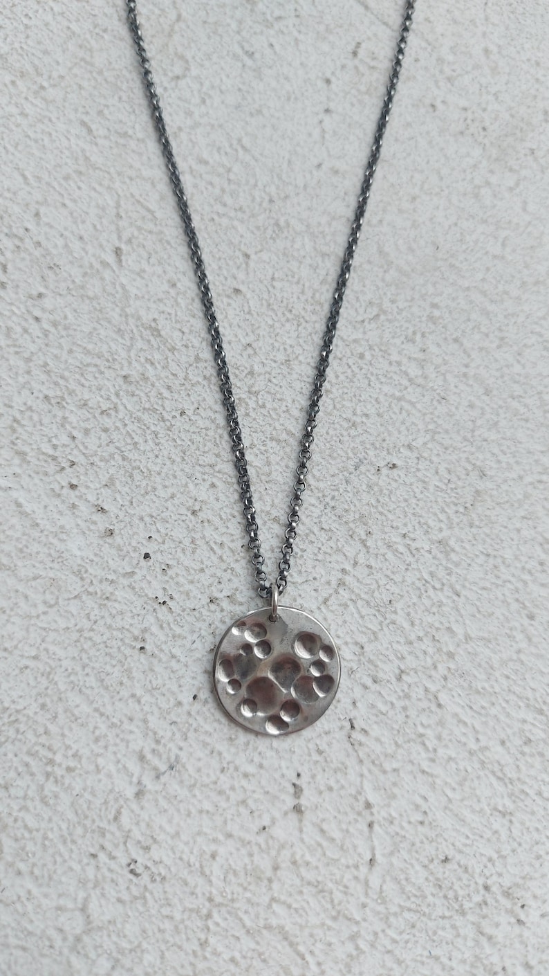 May include: A silver necklace with a round pendant featuring a textured surface with raised circles.