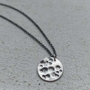 May include: A silver necklace with a round pendant featuring a hammered texture. The pendant has a textured surface with raised circles.