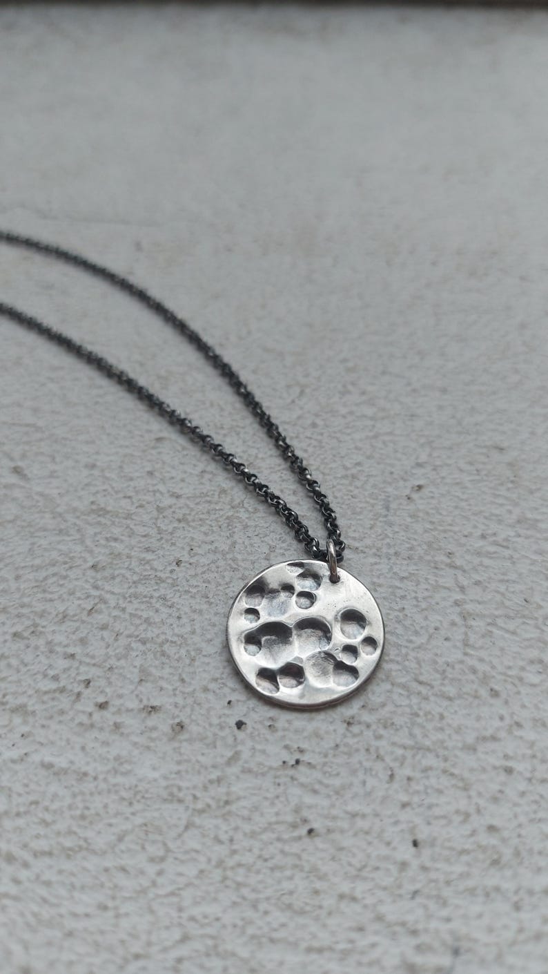 May include: A silver necklace with a round pendant featuring a hammered texture. The pendant has a textured surface with raised circles.