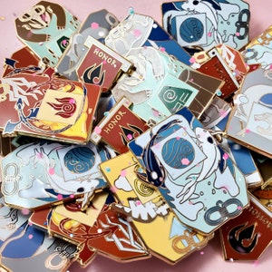 May include: A collection of enamel pins with various designs. Some pins feature a koi fish, others have the word "HONOR" with a flame, and some have symbols. The pins are in shades of blue, red, gold, and white.