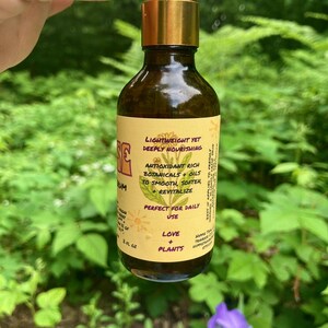 May include: A brown glass dropper bottle with a gold collar and white dropper top. The yellow label features a botanical illustration and text including Lightweight Yet Deeply Nourishing, Antioxidant Rich Botanicals + Oils, and 2 fl oz.