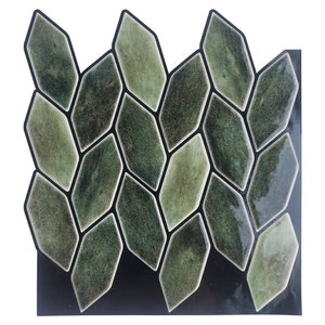 Peut inclure: Une feuille de carreaux décoratifs avec un motif répétitif de pièces vertes en forme de losange. Chaque carreau a une finition brillante et est souligné en noir. Les carreaux sont disposés sur un support noir.