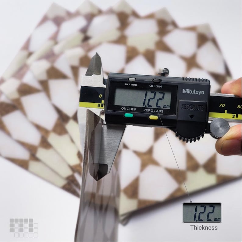 K&ouml;nnte beinhalten: Ein digitaler Messschieber misst die Dicke eines Stapels gemusterten Papiers. Das Messger&auml;t zeigt einen Wert von 1,22 mm an. Das Papier hat ein geometrisches Design in Braun- und Wei&szlig;t&ouml;nen.