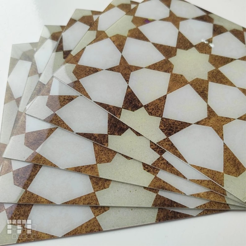 K&ouml;nnte beinhalten: Ein Stapel dekorativer Glasfliesen mit einem geometrischen Sternmuster. Das Design weist wei&szlig;e, braune und beige Farben auf. Die Fliesen sind f&auml;cherf&ouml;rmig angeordnet und zeigen das sich wiederholende Muster.