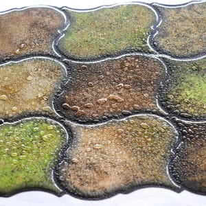 3D peel-and-stick wall tile grid with scalloped square tiles in moss green, brown, and tan for an earthy kitchen backsplash.
