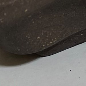 May include: A dark brown ceramic bonsai pot with an irregular, wavy shape and multiple drainage holes. The pot is designed to hold a small tree or plant.