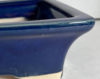 May include: A dark blue square ceramic planter with a white glazed rim and three small feet.
