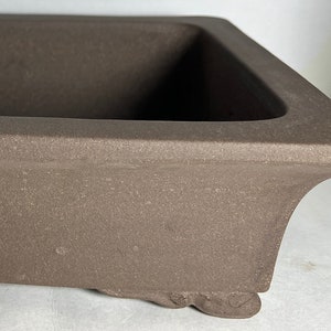 May include: A rectangular brown ceramic bonsai pot with a square opening and four small feet.