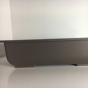 May include: A rectangular brown plastic planter with a slightly curved edge and three small feet on the bottom.