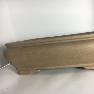 May include: A brown rectangular ceramic bonsai pot with a textured surface and three legs.