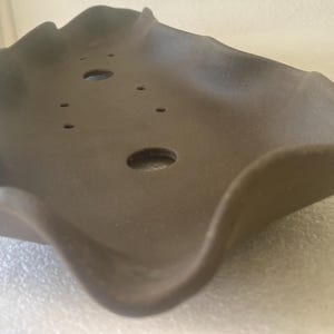 May include: A brown, wavy-edged ceramic bonsai pot with several drainage holes. The pot has a unique, organic shape, and is designed for planting small trees or shrubs. The pot is made of a durable material and is suitable for outdoor use.