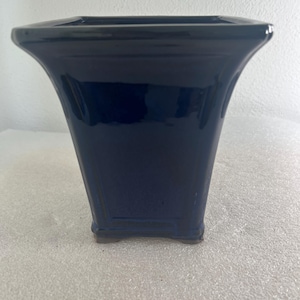 May include: A navy blue ceramic vase with a glossy finish. The vase has a square base that widens towards the top, with a flared rim. The vase is approximately 8 inches tall.