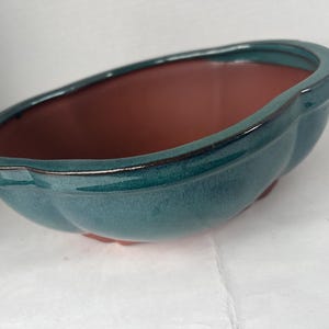 May include: A teal ceramic planter with a scalloped edge and a reddish-brown interior. The planter has a glossy finish and a rounded shape, suitable for small plants or succulents.