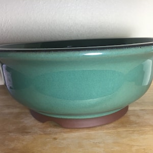 May include: A green ceramic bonsai pot with a brown base. The pot has a smooth, glossy finish.