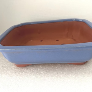 May include: A rectangular bonsai pot with a light blue exterior and a reddish-brown interior. The pot has a slightly raised rim and small feet. The pot is approximately 12 inches long, 9 inches wide, and 3 inches tall.