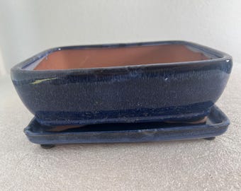May include: A rectangular ceramic bonsai pot with a deep blue glazed exterior and a smooth, light terracotta-colored interior. The pot sits on a matching rectangular blue glazed saucer with small feet, designed to catch excess water drainage.