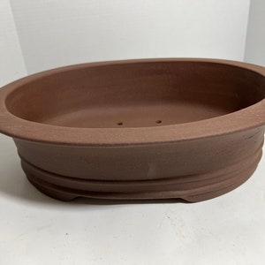 May include: A brown oval ceramic bonsai pot with a textured surface and drainage holes.