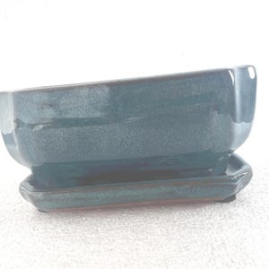 May include: A rectangular teal ceramic bonsai pot with a glossy finish and a matching rectangular drip tray. The pot features slightly rounded corners and a smooth, reflective surface that transitions between shades of deep blue and green.