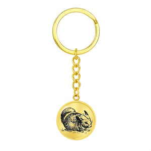 May include: Gold-colored keychain with a round metal charm featuring a black and white illustration of a chinchilla.