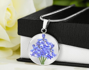 May include: A silver necklace with a round pendant featuring a cluster of blue bellflowers. The pendant is on a white background.