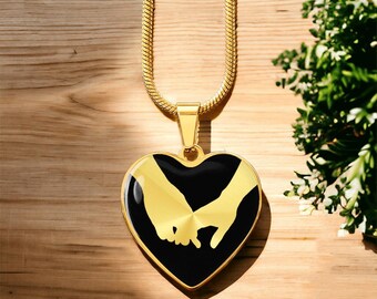 Può includere: Collana d'oro con un ciondolo a forma di cuore nero che presenta la silhouette di due mani che si tengono.