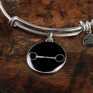 May include: A silver expandable bangle bracelet with a black round charm featuring a white silhouette of a horse bit.