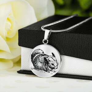 May include: A silver necklace with a round pendant featuring a black and white illustration of a chinchilla. The chinchilla is sitting on the ground and looking to the right.