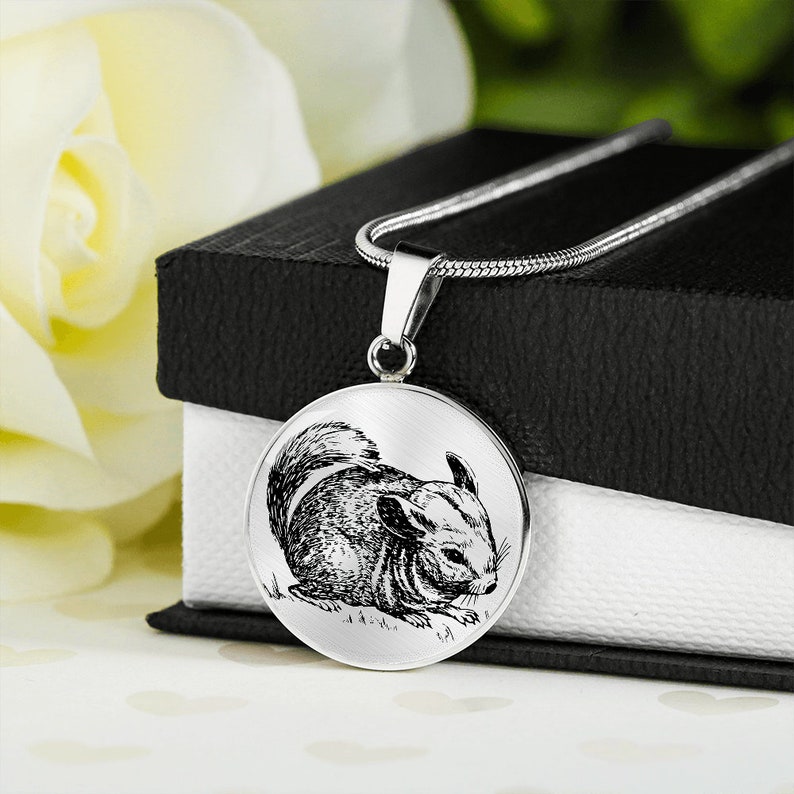 May include: A silver necklace with a round pendant featuring a black and white illustration of a chinchilla. The chinchilla is sitting on the ground and looking to the right.