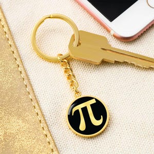 May include: Gold keychain with a black circle charm featuring the mathematical symbol pi in gold.