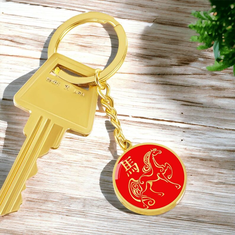 May include: Gold-coloured key and keyring with a red circular charm. The charm features a gold horse illustration and Chinese characters. The key says "MADE IN USA".