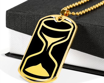 May include: A gold dog tag necklace with a black hourglass design. The necklace is on a black box with a white interior.