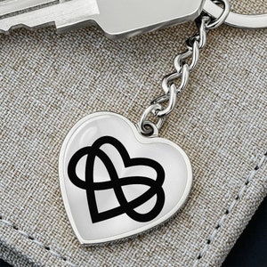 Puede incluir: Llavero de corazón plateado con un diseño de símbolo de infinito negro. El llavero está unido a una cadena plateada.
