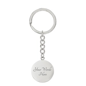 May include: A silver-coloured keychain with a round pendant. The pendant is attached to a chain and a key ring. The pendant has the text "Your Words Here" engraved on it. The keychain is designed to hold keys.