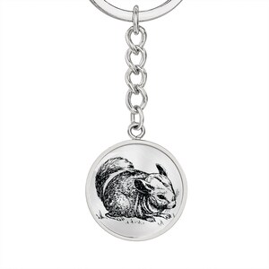 May include: A silver keychain with a round charm featuring a black and white line drawing of a chinchilla.