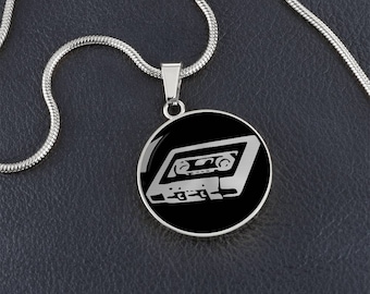 May include: A silver chain necklace with a black circular pendant featuring a white outline of a cassette tape.