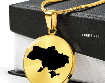 Könnte beinhalten: Goldkette mit einem runden Anhänger, der eine schwarze Silhouette der Karte der Ukraine zeigt. Der Anhänger befindet sich auf einer schwarzen Box mit dem aufgedruckten Text "FREE BOX!"
